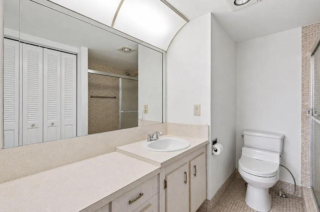 Full-width vanity mirror, integrated sink, built-in cabinetry with pulls, louvered bi-fold closet doors, and a shower enclosure with a sliding glass door