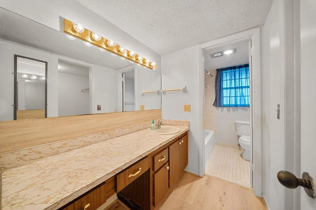 Extended vanity with integrated sink, wood-finish cabinetry, and a full-width mirror with overhead light bar