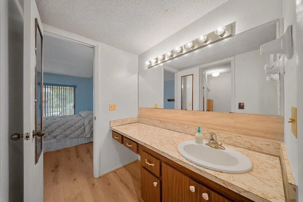 Extended vanity with a single basin sink, wood-finish cabinetry, and a full-width mirror with overhead lighting