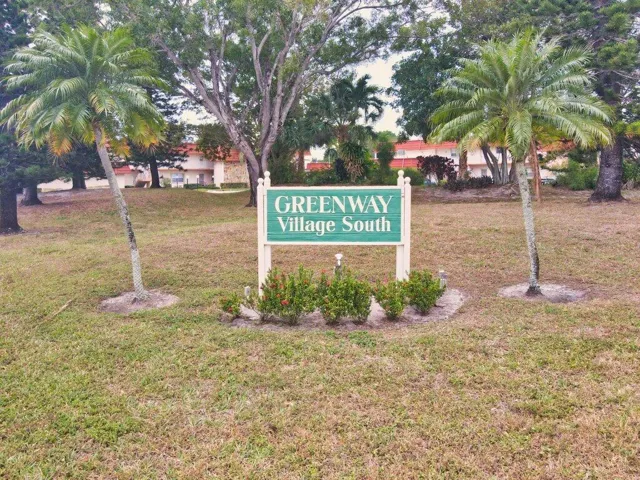 Greenway Village South community sign with a landscaped base, flanked by mature palm trees and established foliage