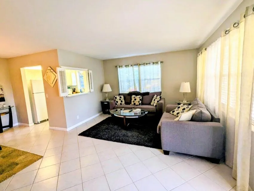 Expansive tiled flooring throughout, a pass-through window with louvered shutters, and multiple windows providing ambient light