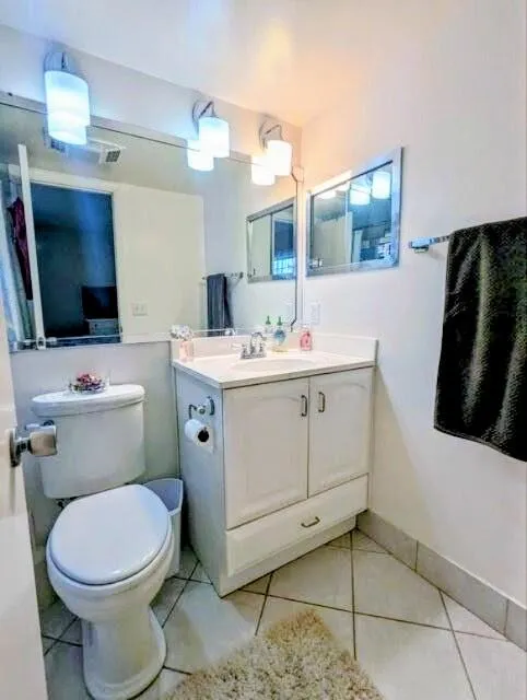 White vanity with cabinet storage, coordinating white toilet, dual wall-mounted mirrors, and tiled flooring