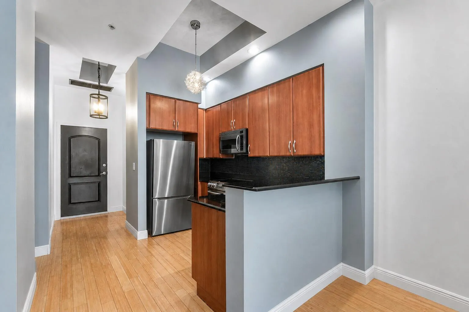Hardwood flooring, wood cabinetry, stainless steel appliances, black countertops, and recessed lighting