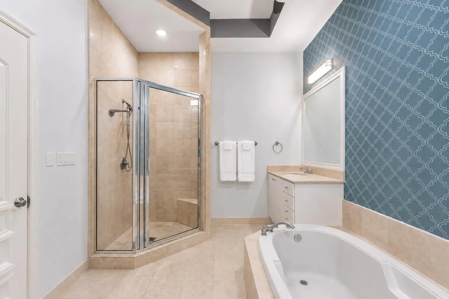 Tiled walk-in shower with a built-in bench, single vanity with a light-toned countertop, and a built-in soaking tub