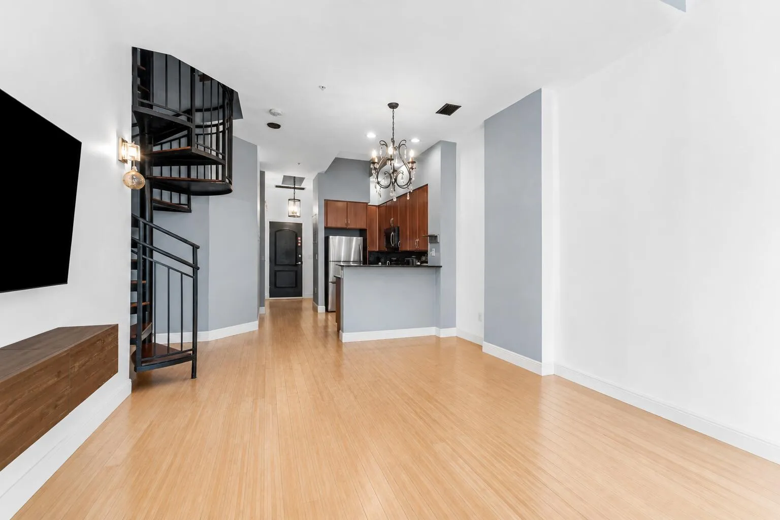 Open-concept living space featuring wood-finish flooring, a spiral staircase with metal railings, and a kitchen with wood cabinetry and stainless steel appliances
