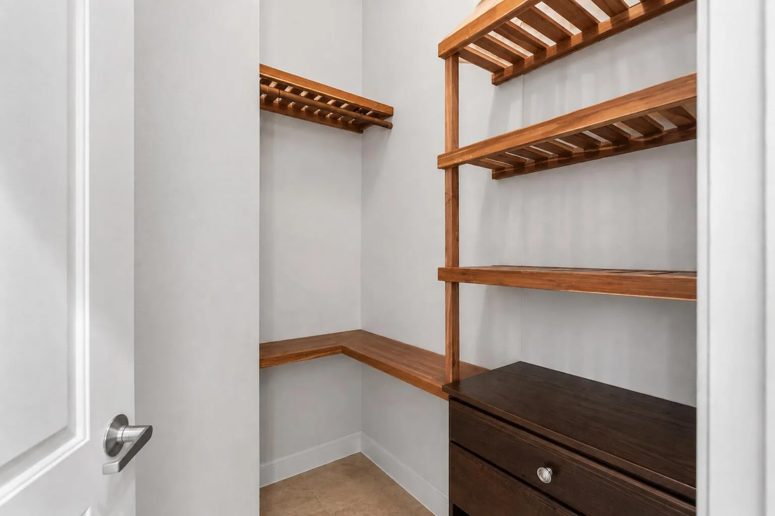 Built-in wood-finish shelving, corner wood-finish counter space, integrated dark wood-finish cabinet with drawer, and tile flooring