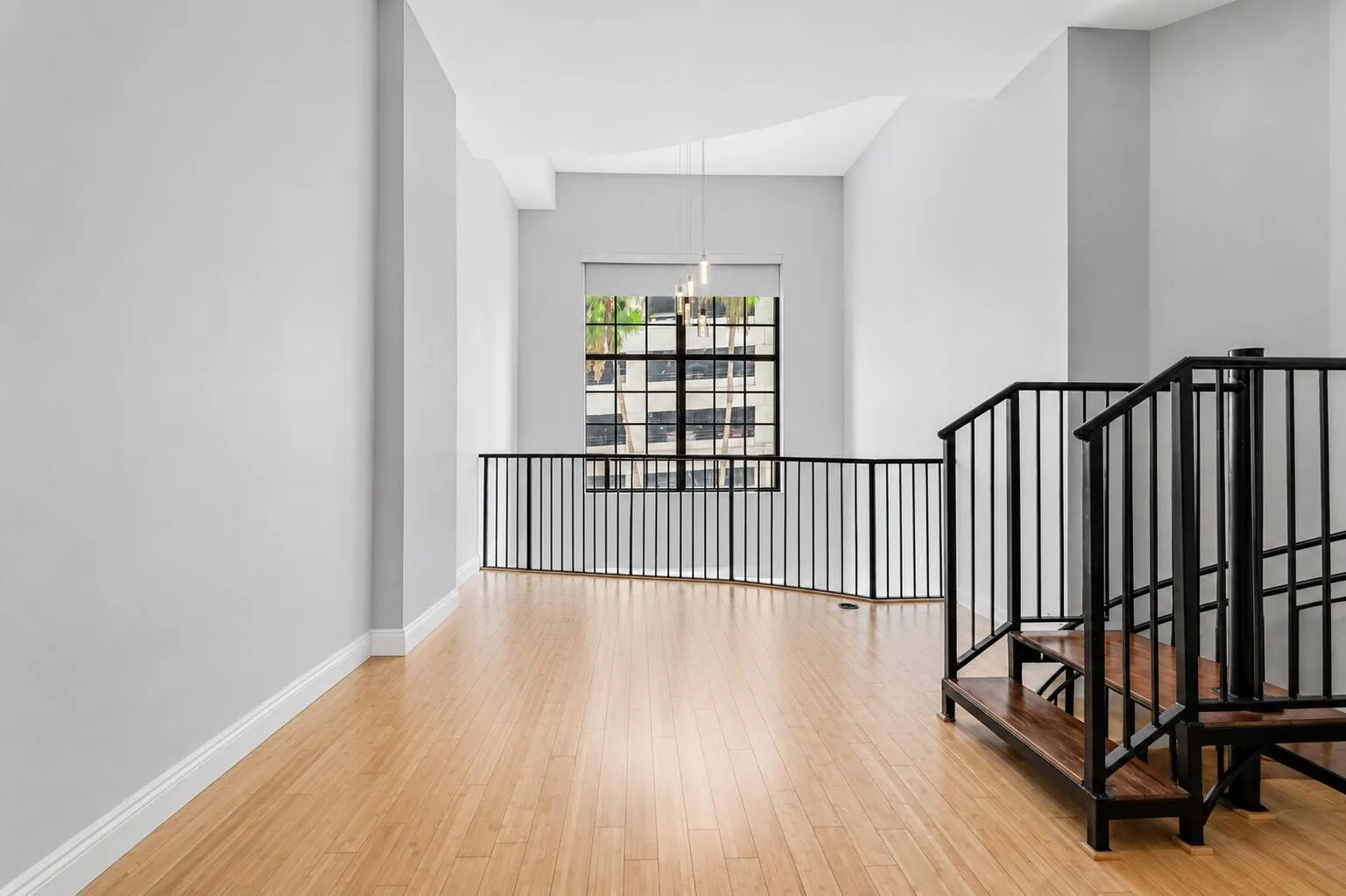 Wood-finish flooring, high ceilings, loft-style railing, large window, and suspended light fixture