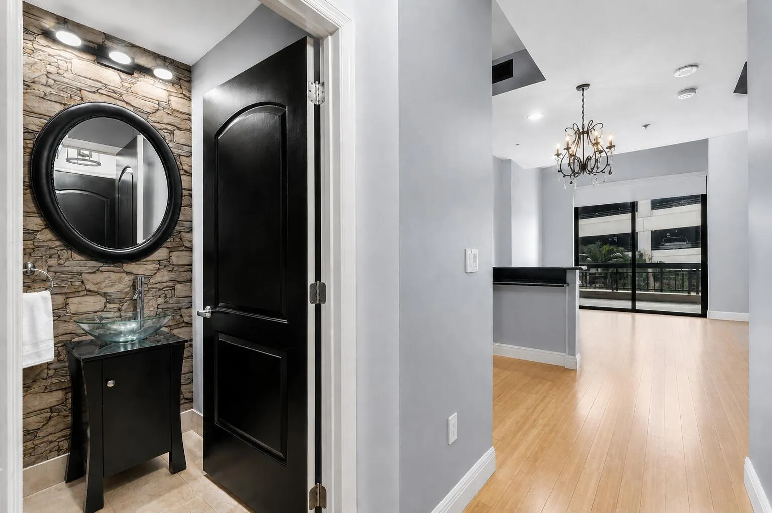 Stone accent wall with a circular mirror, glass vessel sink, and a black vanity