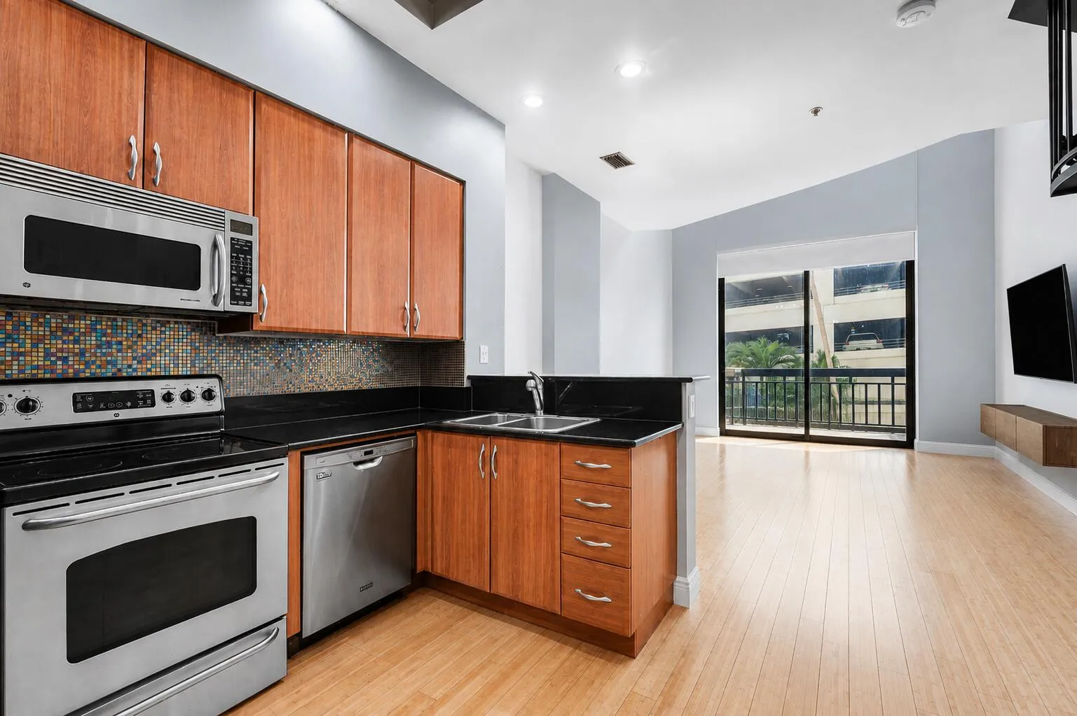 Kitchen featuring wood cabinetry, stainless steel appliances, black countertops, and a tiled backsplash