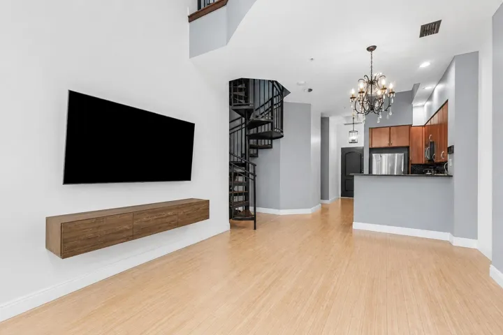 Light wood-finish flooring, a spiral staircase with metal railings, and a kitchen featuring wood cabinetry, stainless steel appliances, and a chandelier