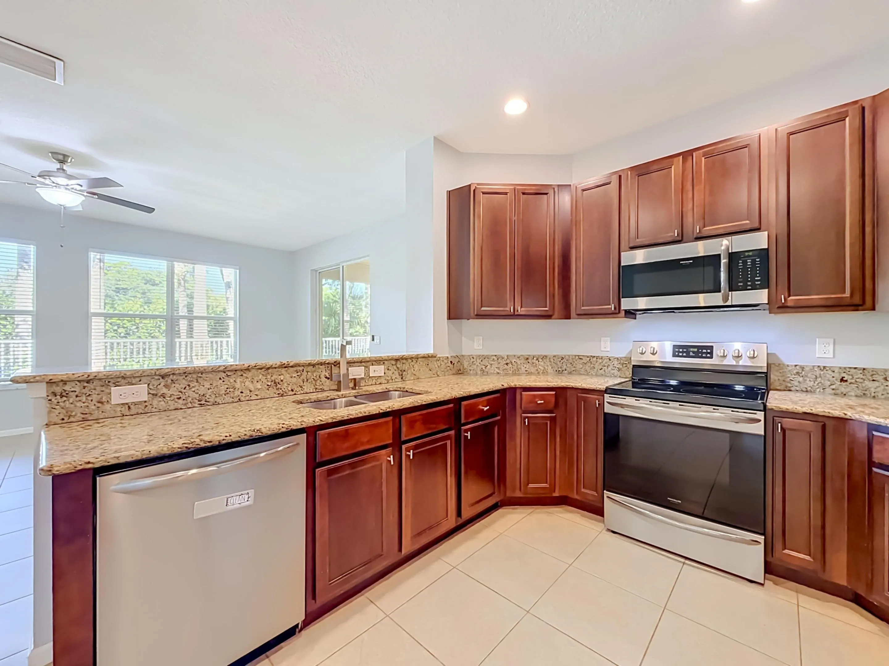 Kitchen featuring stainless steel appliances, wood cabinetry, stone countertops, a double basin sink, and tile flooring