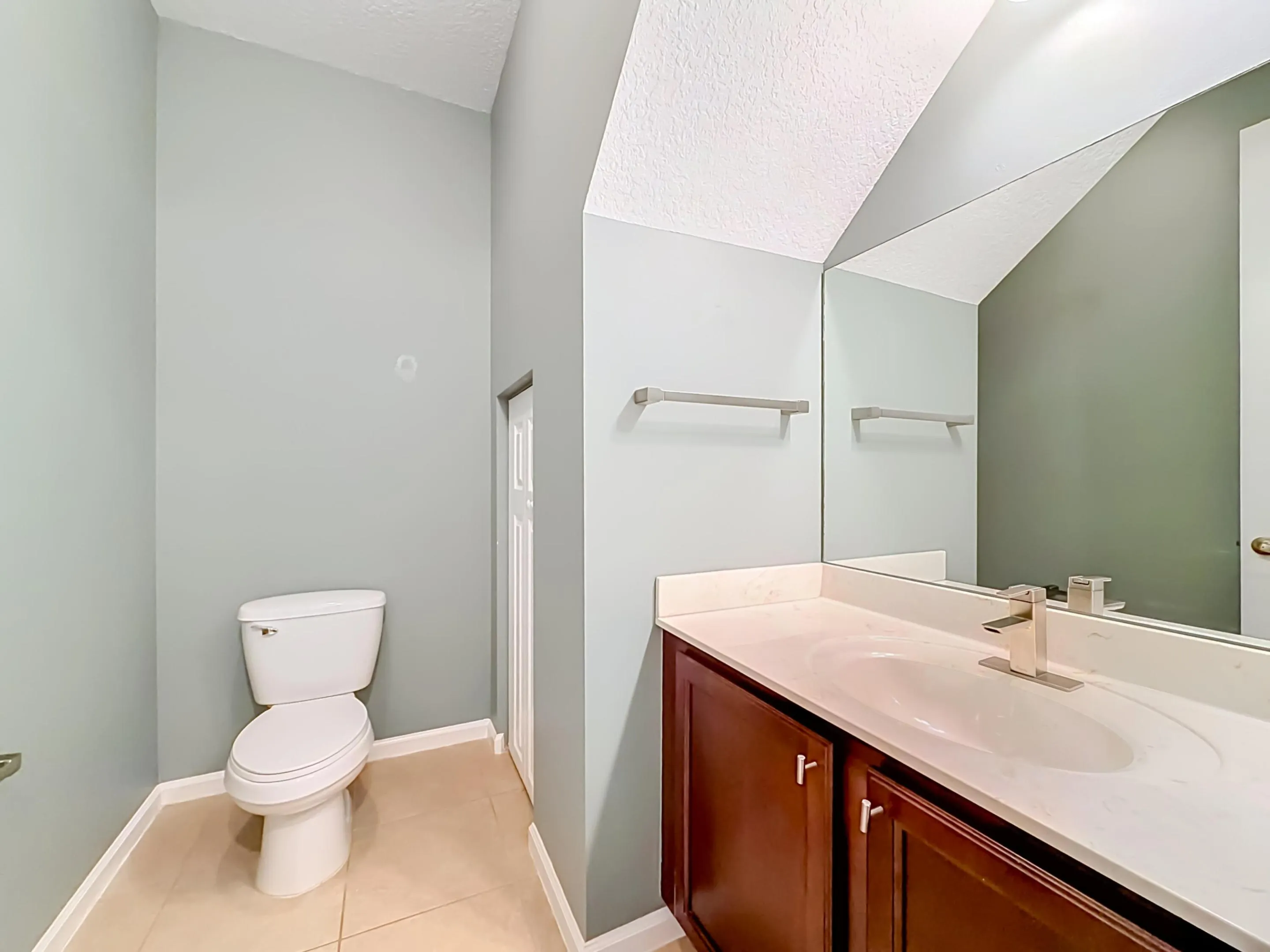 Vaulted ceiling, full vanity mirror, integrated sink, wood-finish cabinetry, and tiled flooring