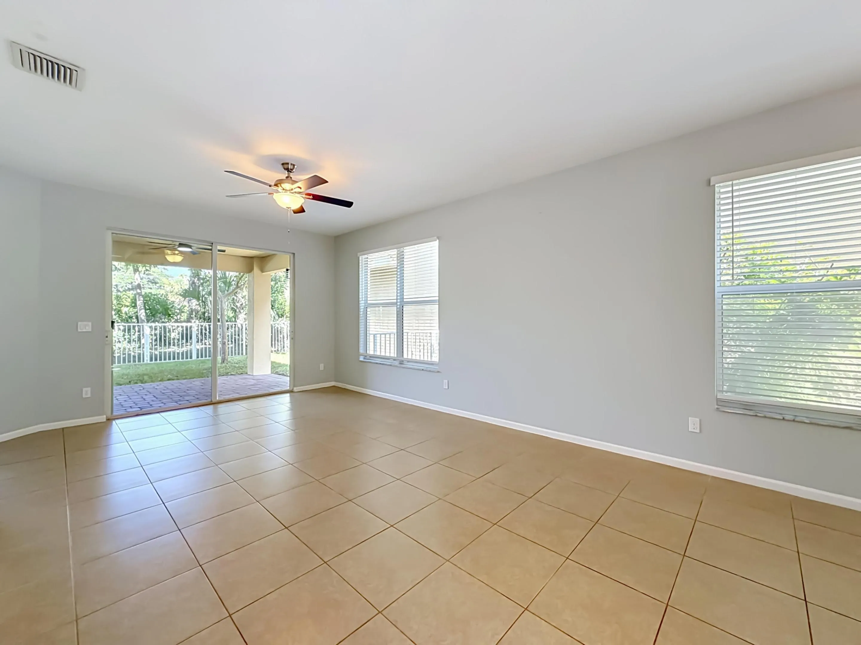 Neutral wall paint, tile flooring, ceiling fan with integrated lighting, sliding glass doors to outdoor patio, and multiple windows