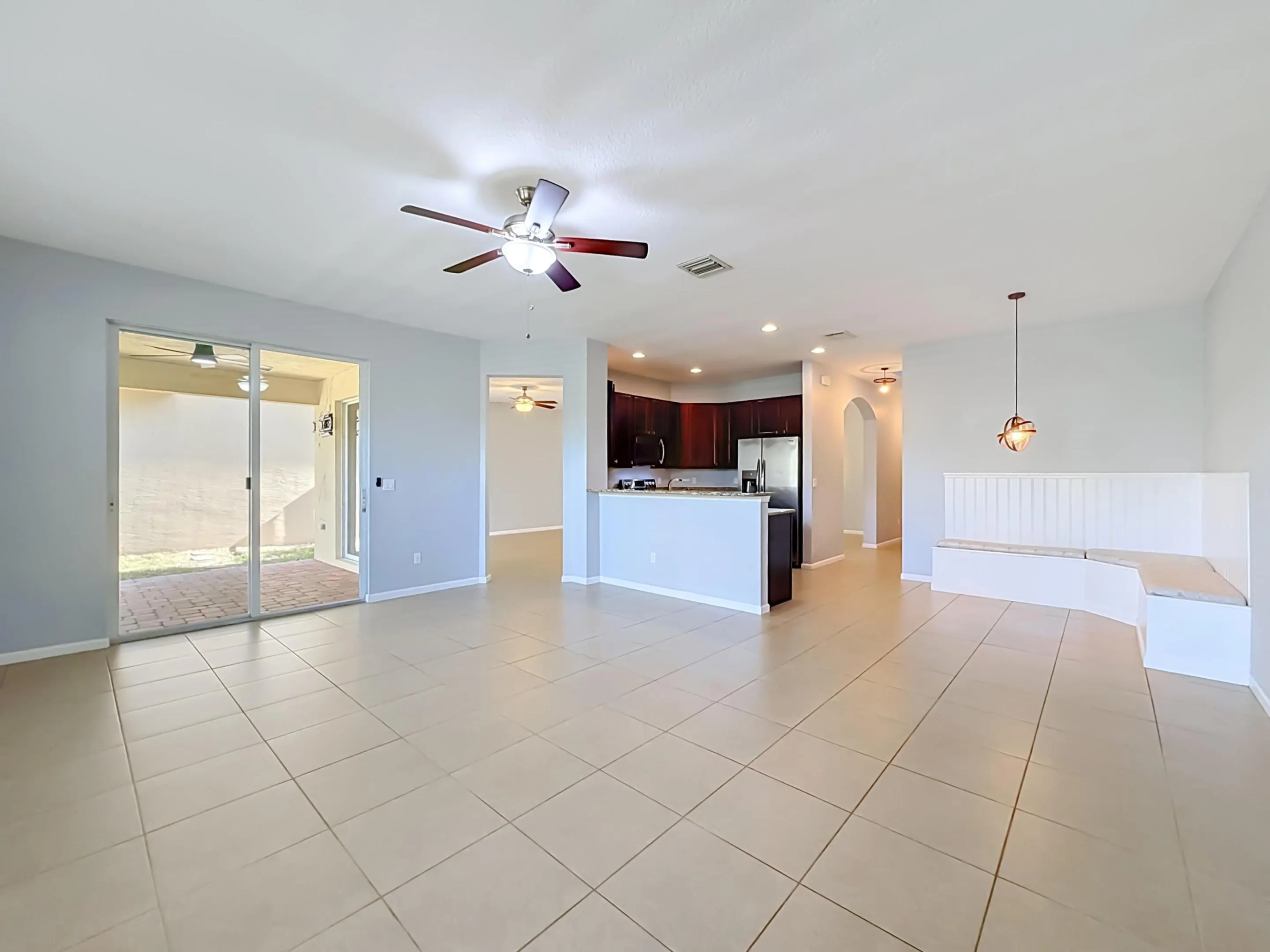 Open-concept living space with tile flooring, a ceiling fan, and sliding glass doors to a paved patio