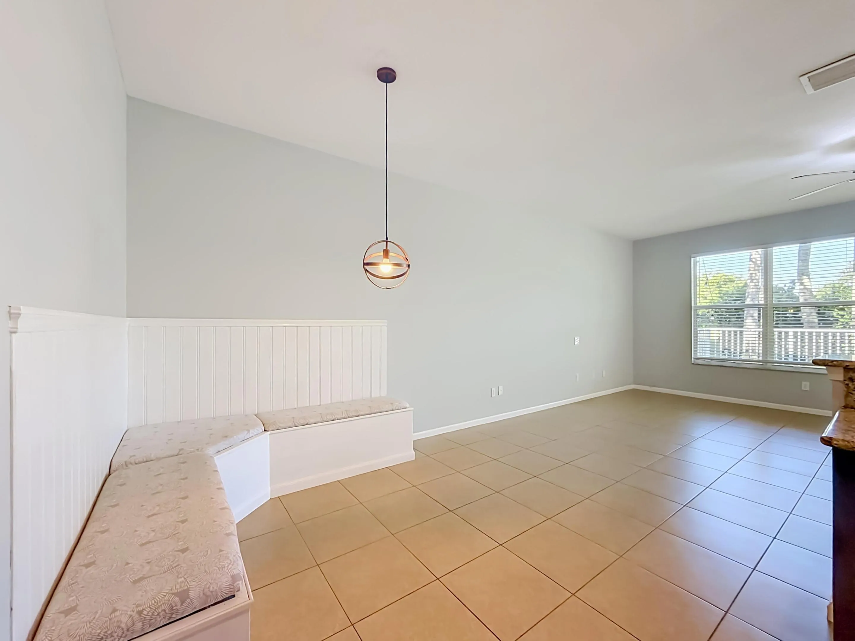 Vaulted ceiling, contemporary pendant lighting, built-in banquette seating with storage, tile flooring, and a large window