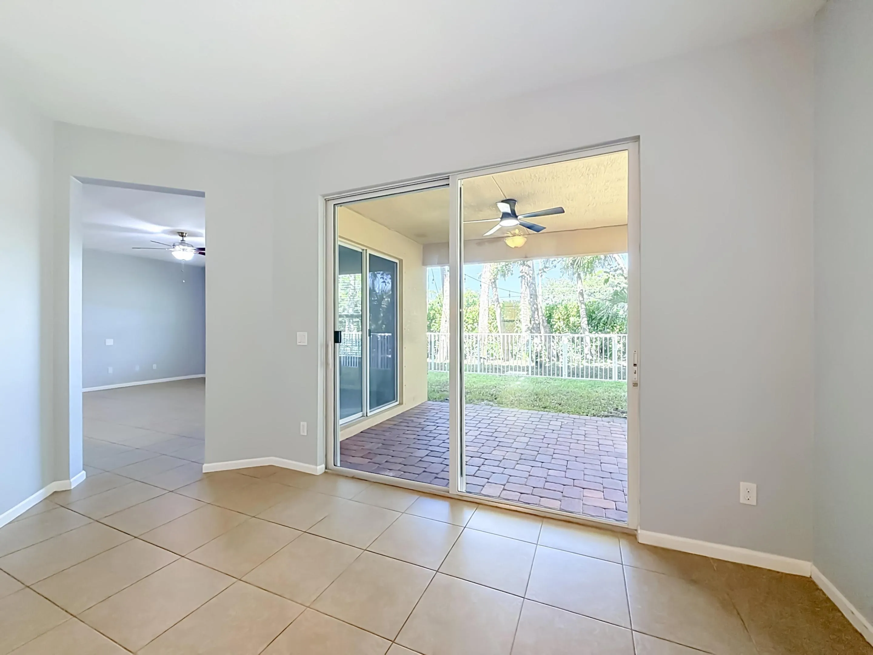 Tile flooring, sliding glass doors, brick paver patio, ceiling fan, and backyard with fencing