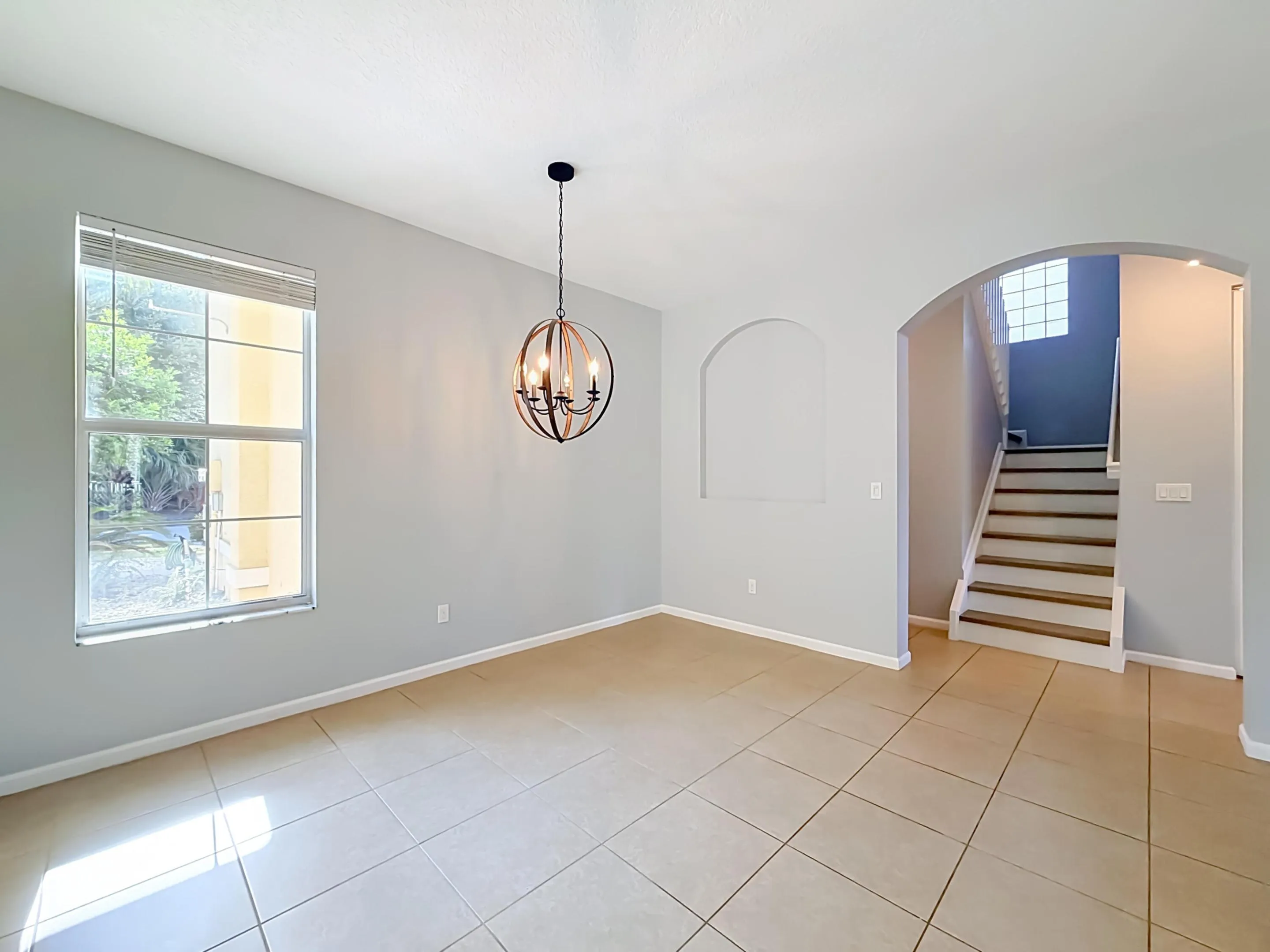 Expansive tiled flooring, arched doorway, recessed wall niche, and modern spherical chandelier
