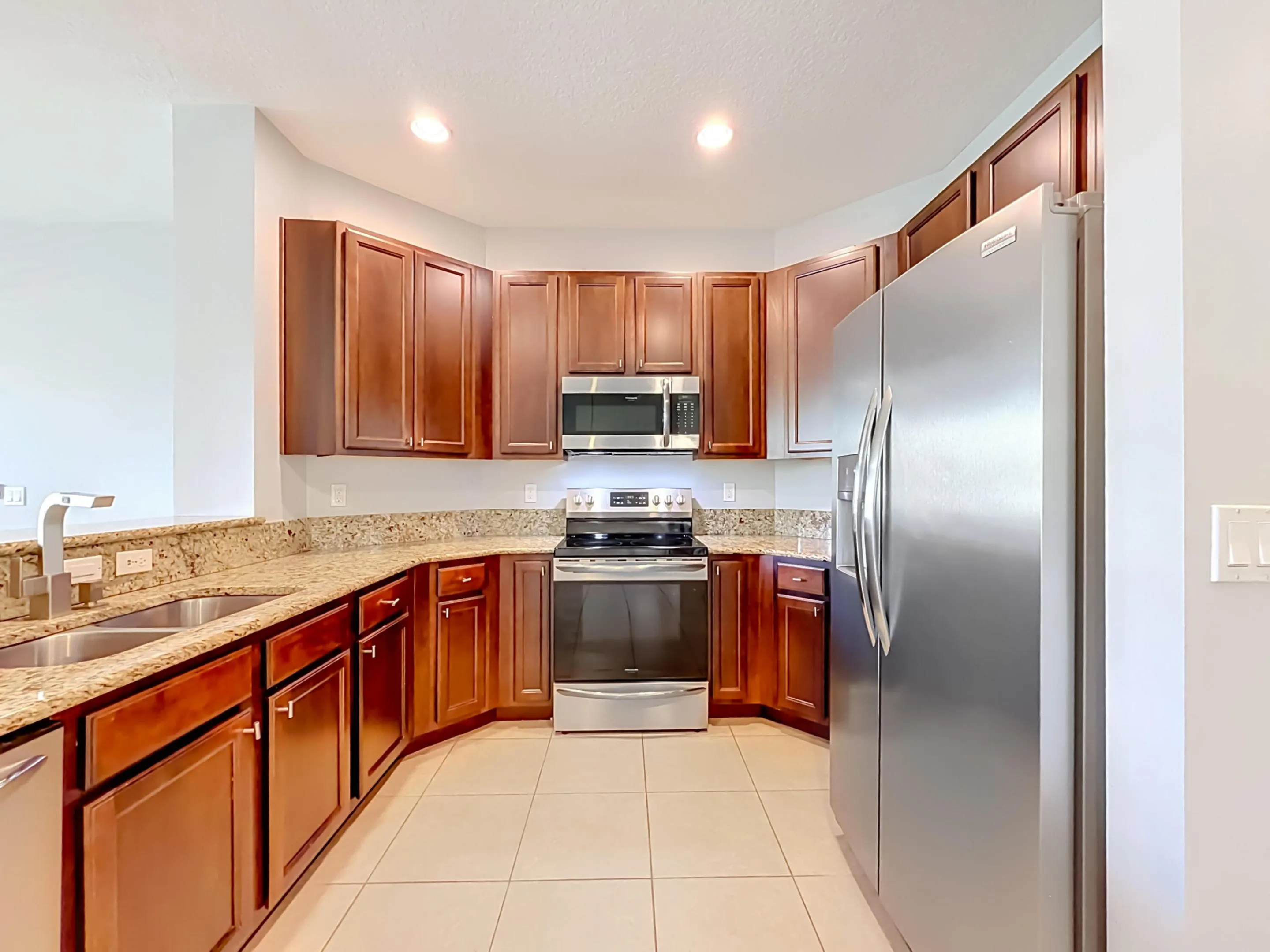 Kitchen featuring a double basin stainless steel sink, granite countertops, tile flooring, rich wood-finish cabinetry, and stainless steel appliances