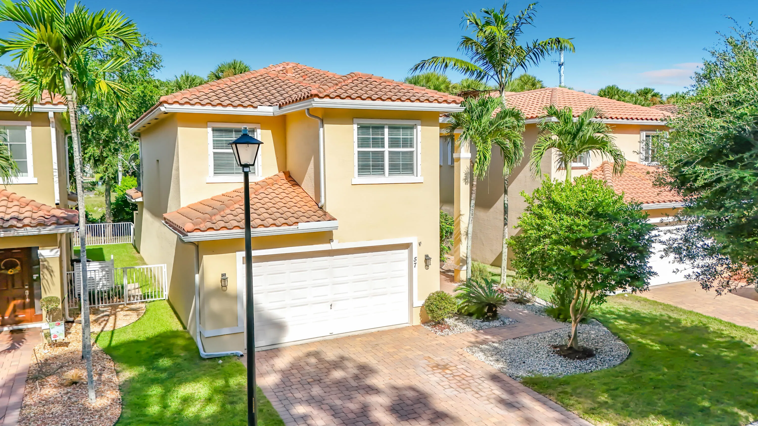 Stucco exterior with a terracotta tile roof, paver driveway, attached garage, and established landscaping