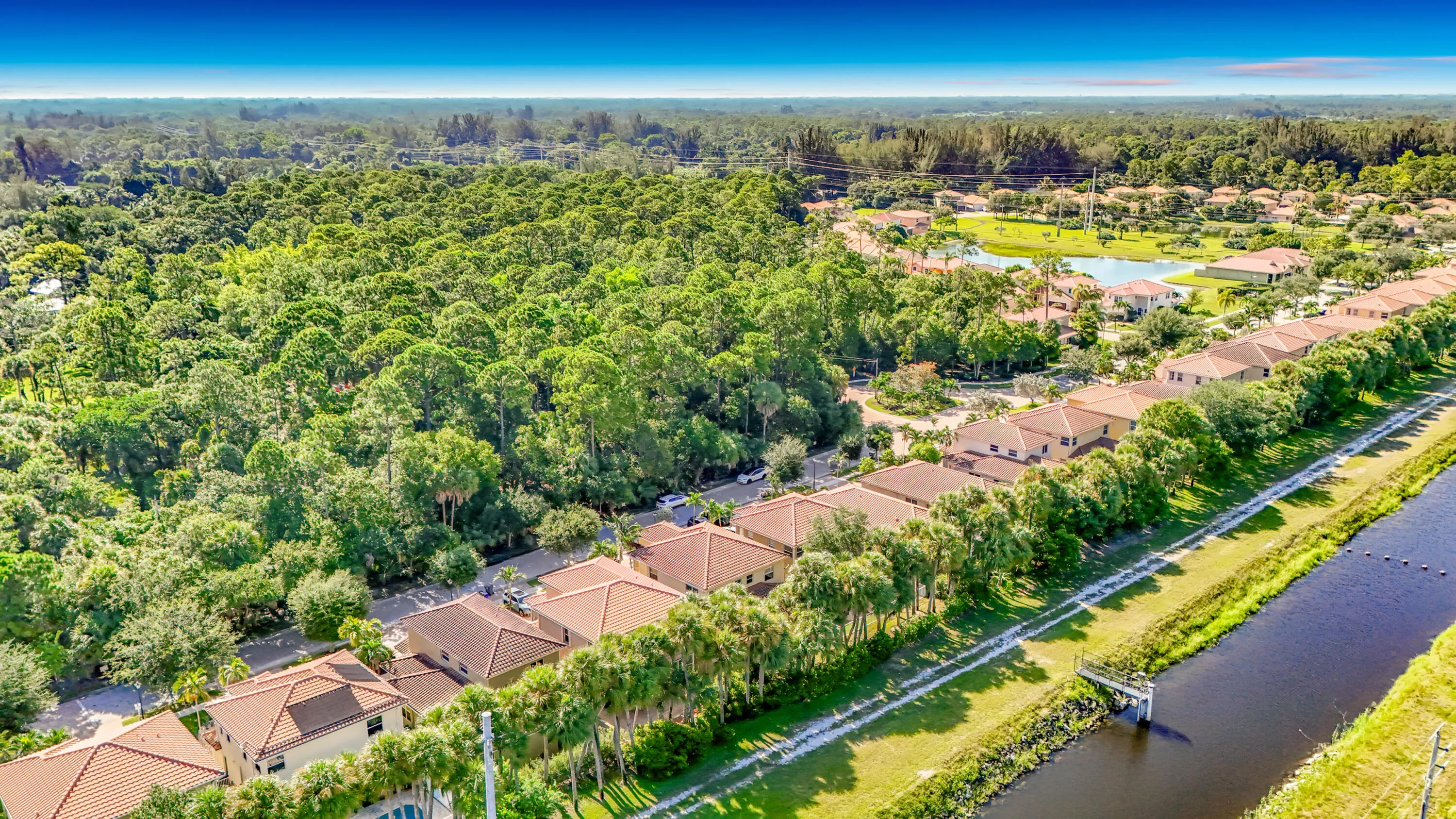 Residential properties with barrel tile roofs situated alongside a waterway with lush, mature landscaping