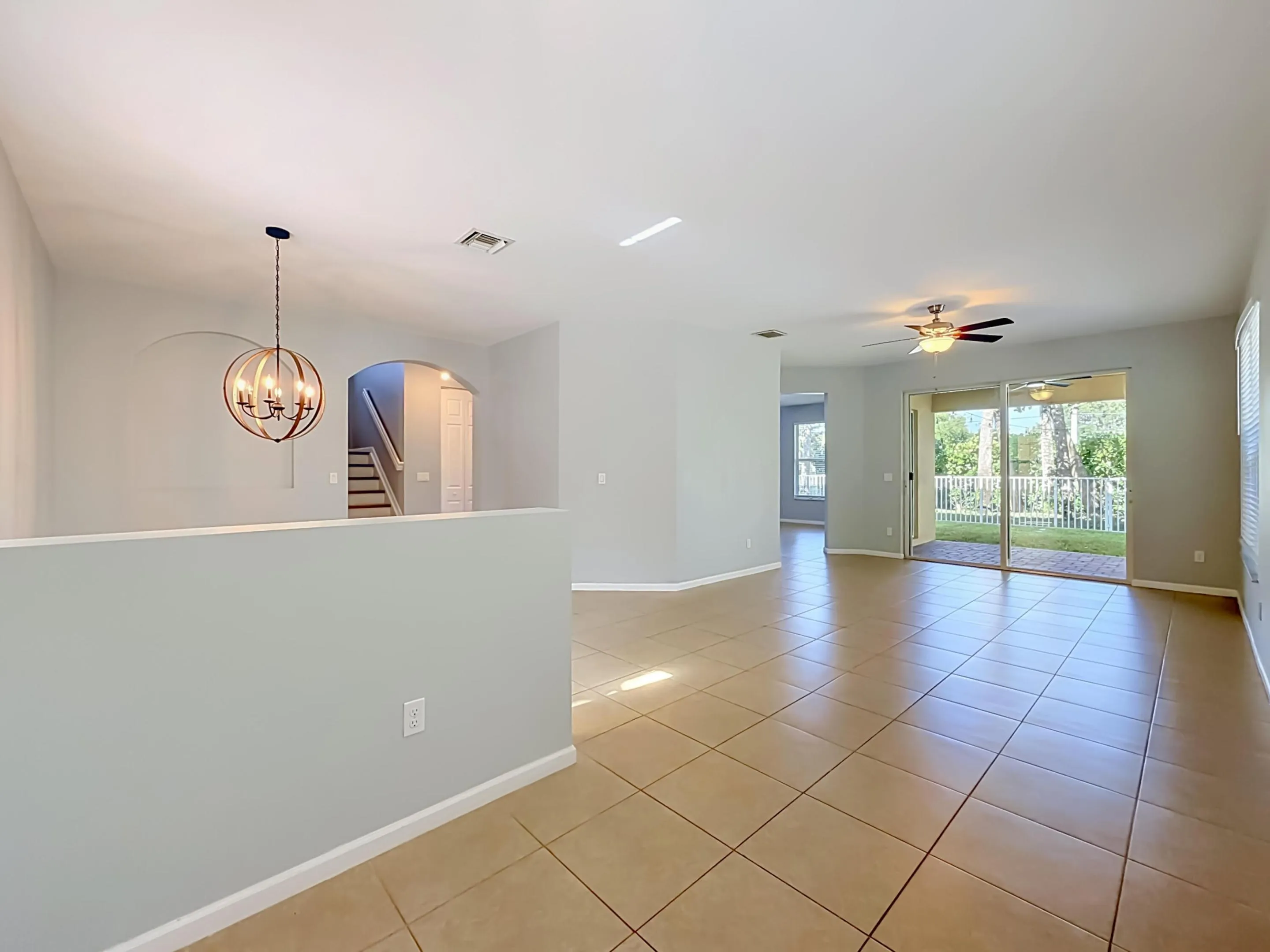 Expansive open-concept living area featuring large format tile flooring, a contemporary spherical chandelier, and a ceiling fan with integrated lighting