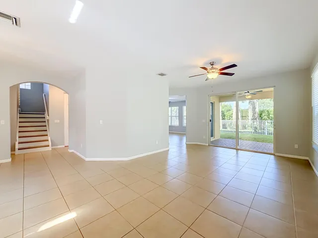 Tile flooring throughout, arched entryway, staircase with wood treads, sliding glass doors to outdoor patio, and a ceiling fan with integrated lighting