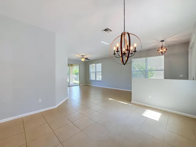 Open concept interior featuring tile flooring, dual contemporary chandeliers, a ceiling fan, and large windows with blinds