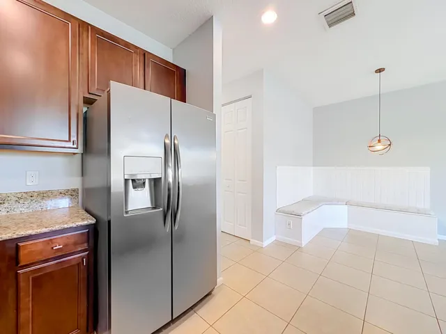 Stainless steel refrigerator, wood cabinetry, stone-finish countertop, corner built-in bench seating, and a modern pendant light fixture