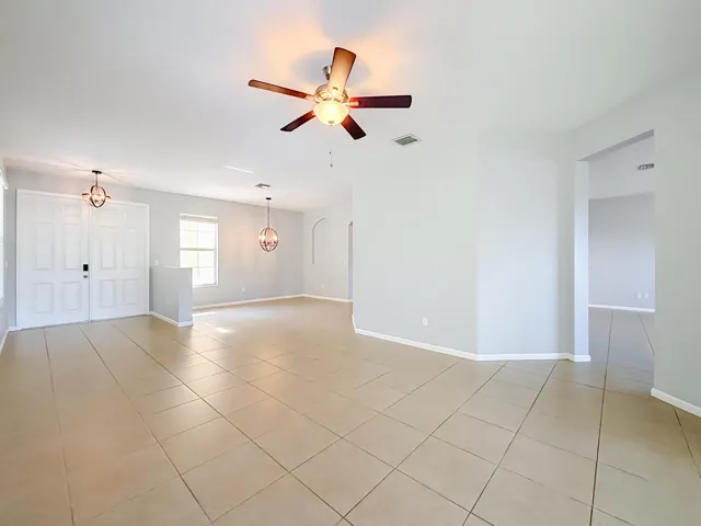 Spacious open-concept living area featuring neutral-toned tile flooring, light gray walls, and a ceiling fan with integrated lighting
