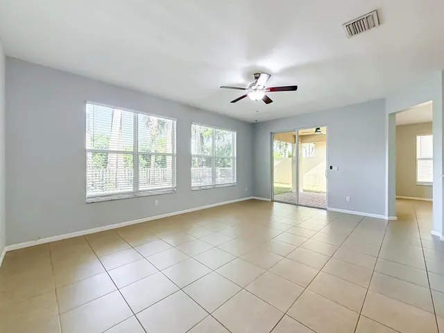 Spacious room featuring tile flooring, multiple windows, a ceiling fan with integrated lighting, and a sliding glass door leading to an outdoor patio