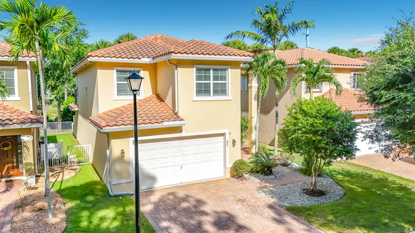 Stucco exterior with a terracotta tile roof, paver driveway, attached garage, and established landscaping