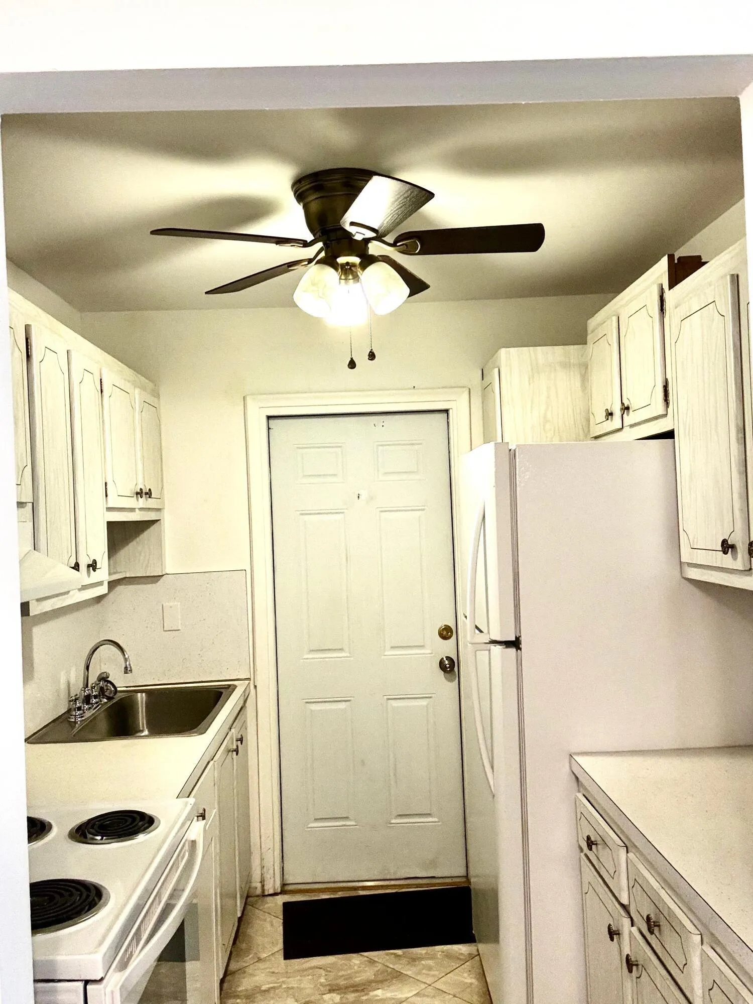 White cabinetry, recessed sink, light-toned countertops, and a ceiling fan with integrated lighting