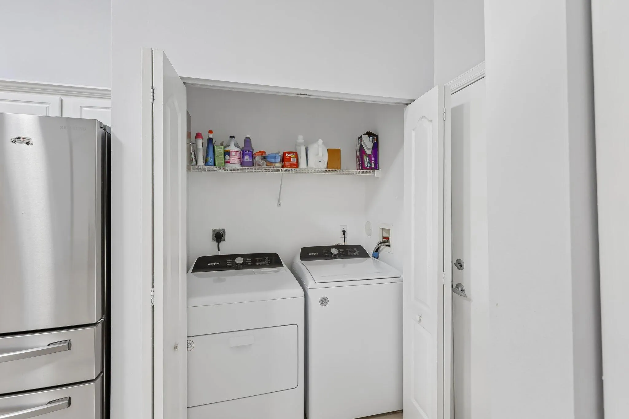 Integrated laundry closet with white appliances and an overhead storage shelf