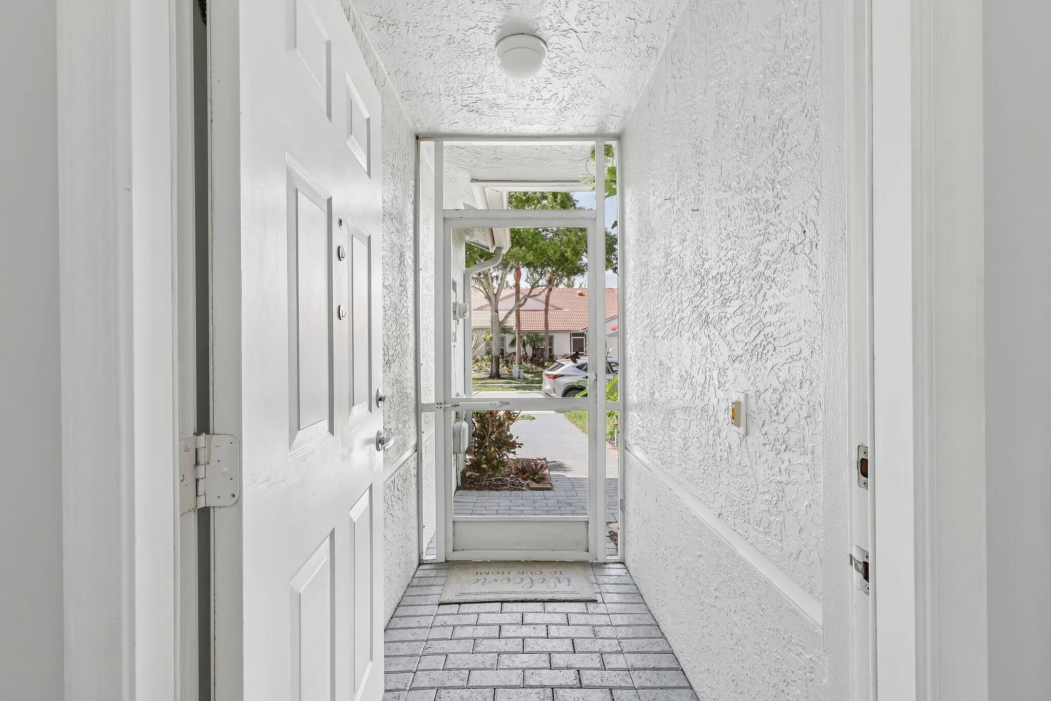 Covered entry with a textured ceiling, brick-patterned flooring, and a screened enclosure