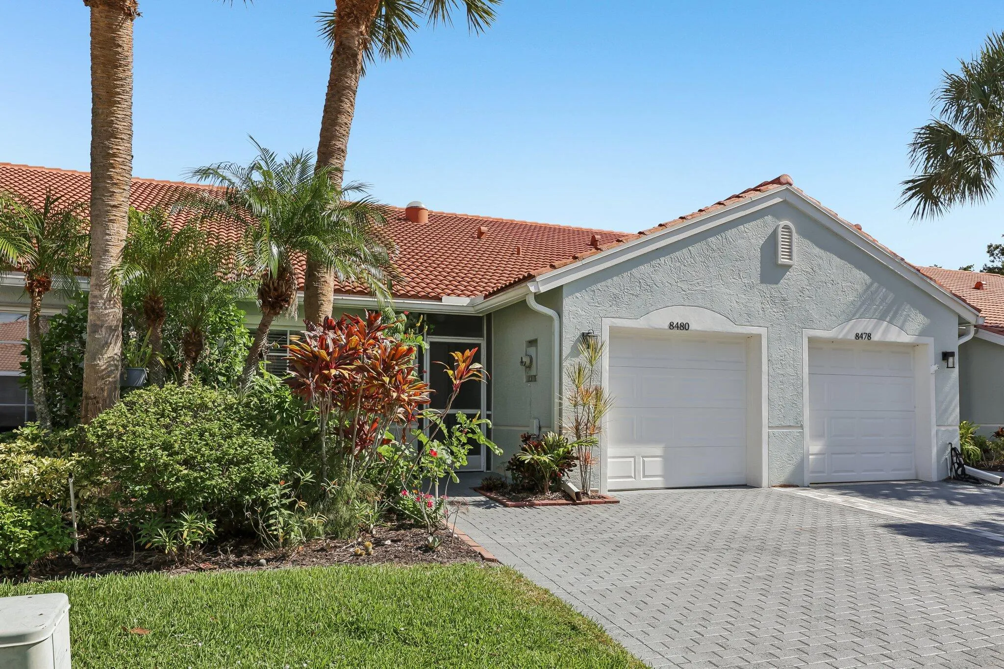 Stucco exterior with a terracotta tile roof, paver driveway, and an attached two-car garage