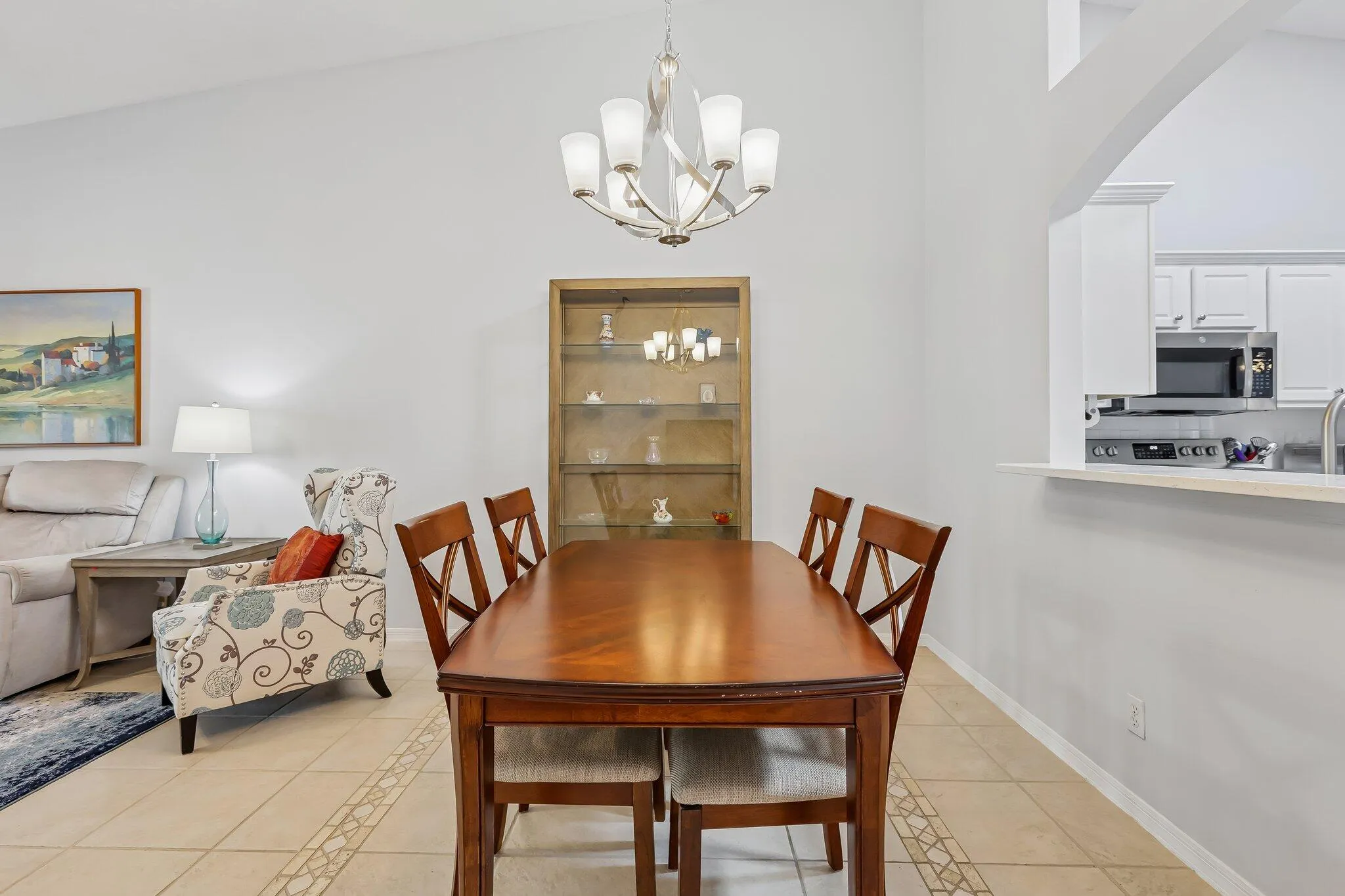 Vaulted ceiling, tiled flooring with decorative inlay, built-in display shelving, built-in kitchen cabinetry, and a kitchen pass-through