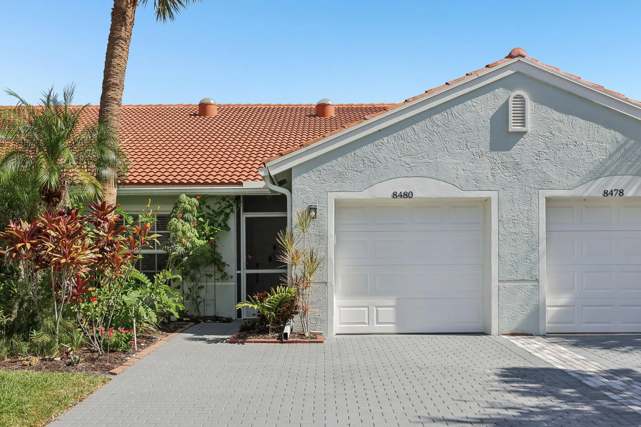 Textured exterior finish, terracotta tile roof, paver driveway, attached garage, and mature landscaping
