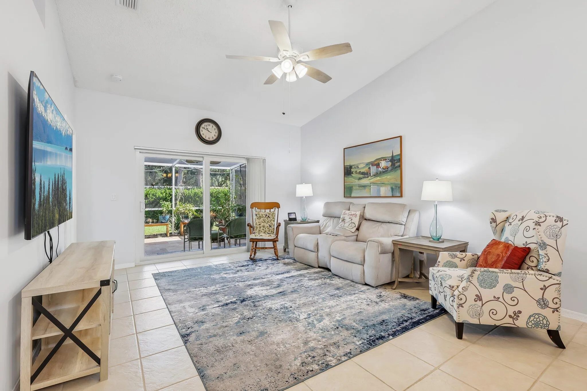Vaulted ceiling, ceiling fan with integrated lighting, tile flooring, and sliding glass doors opening to the exterior