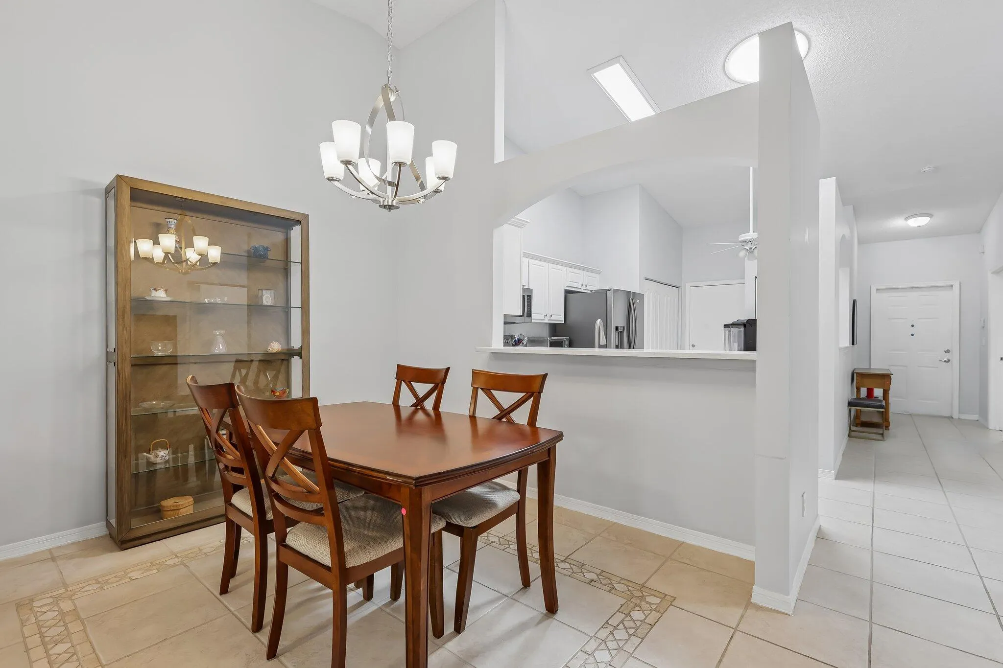 Vaulted ceilings, a contemporary chandelier, a kitchen pass-through, an arched entryway, and tile flooring