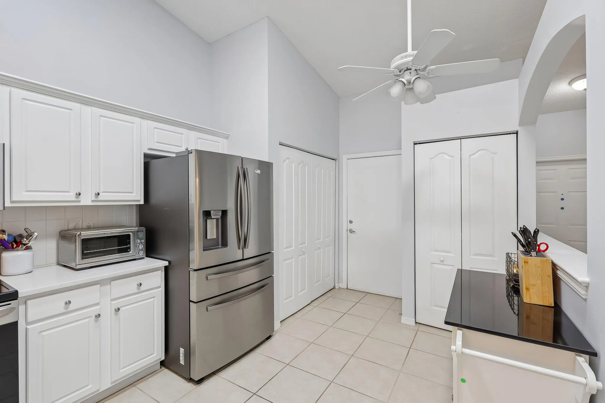 White cabinetry with chrome hardware, stainless steel refrigerator, white tile flooring, and vaulted ceiling with a ceiling fan