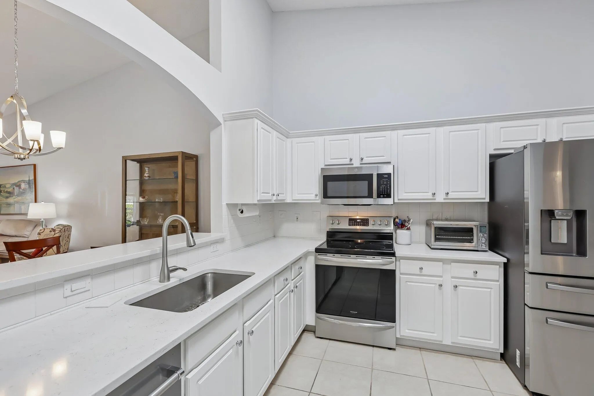 Kitchen featuring white cabinetry, stainless steel appliances, a stainless steel sink with a gooseneck faucet, light-toned countertops, and tile flooring