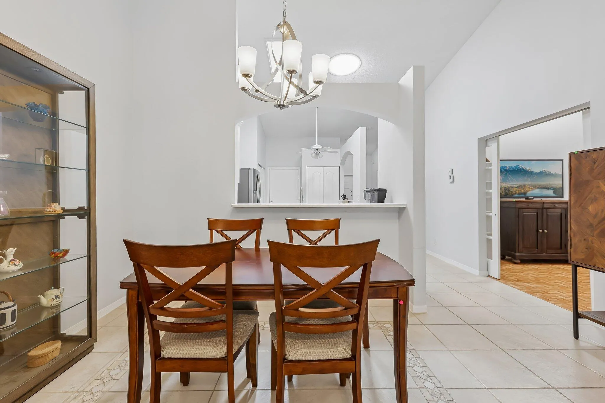 Vaulted ceilings with a central chandelier, tiled flooring, an arched pass-through, a display cabinet with glass shelving, and a cased opening