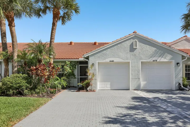 Stucco exterior with a terracotta tile roof, dual garage doors, and a paver driveway