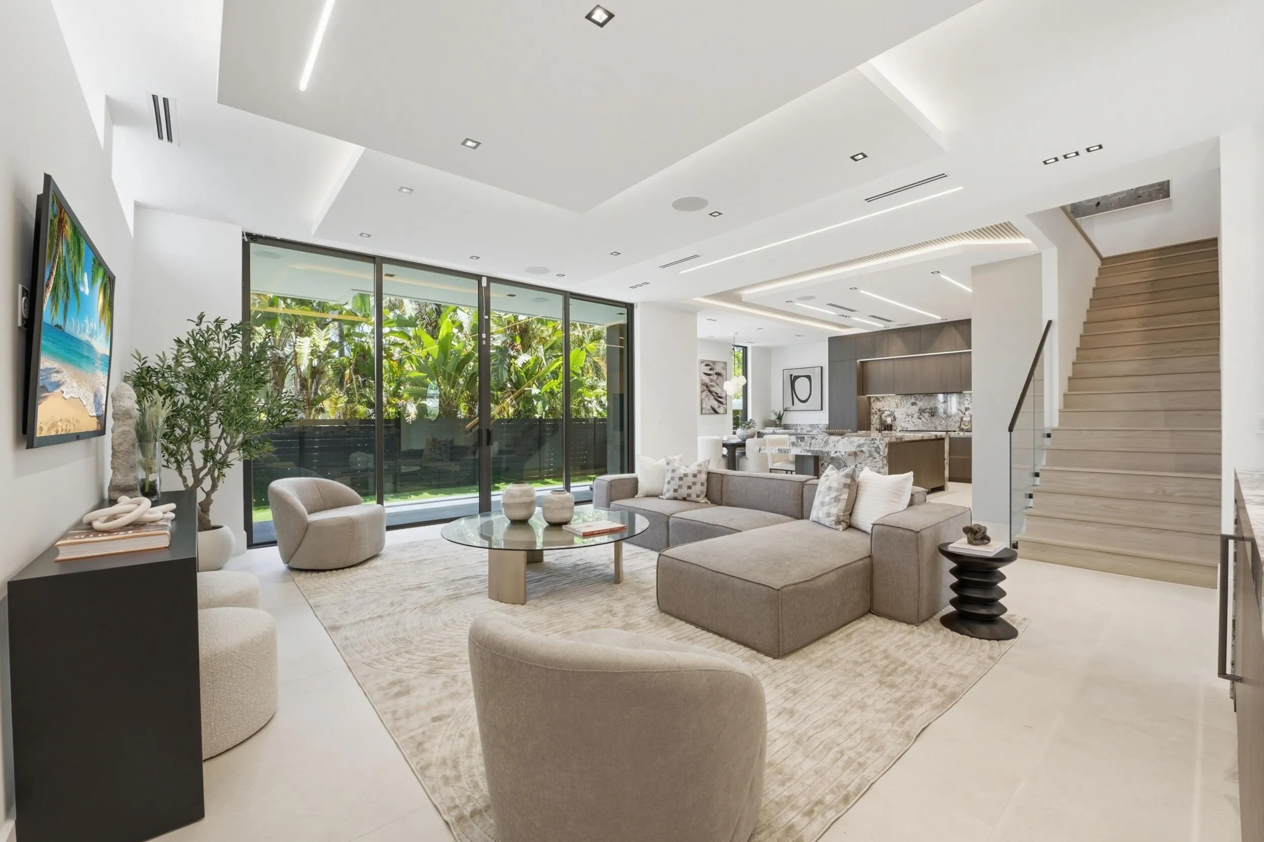Recessed lighting with layered ceiling design, floor-to-ceiling sliding glass doors, light-toned flooring, wood-finish staircase, and open concept living area