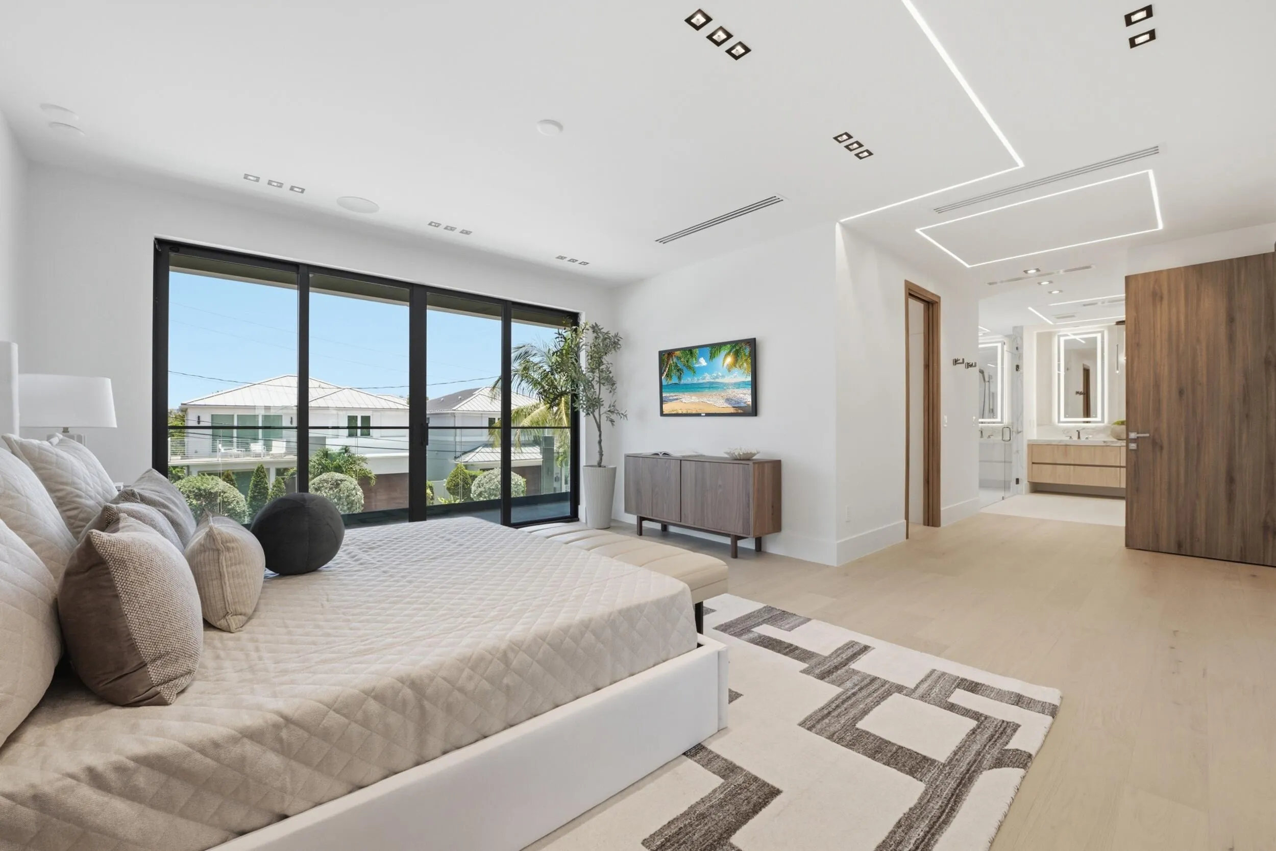 Wide plank wood-finish flooring, recessed ceiling lighting, full-height sliding glass panel door, light wood bathroom vanity with dual sinks, and an integrated lighting fixture