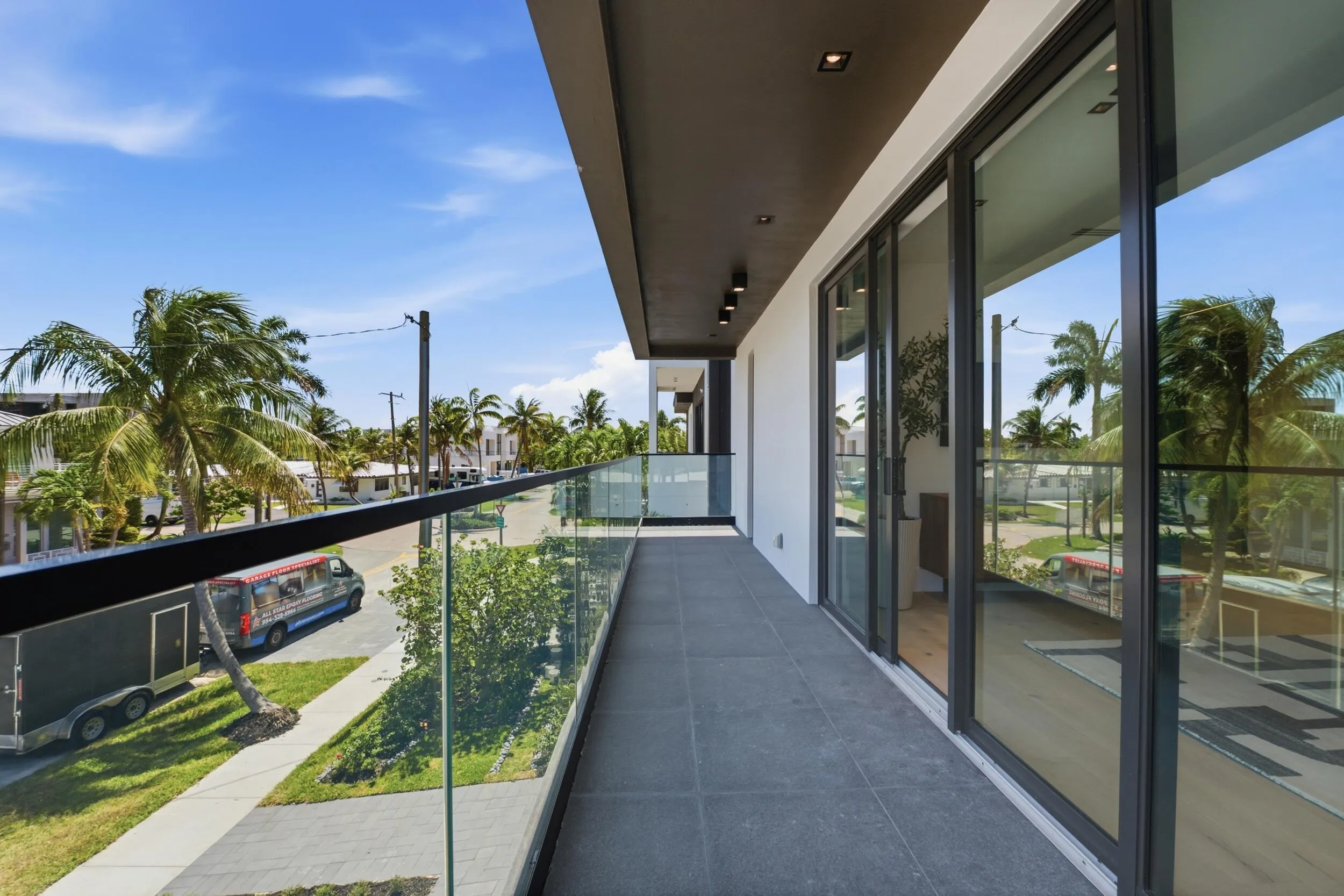 Expansive balcony featuring dark tile flooring, contemporary glass railings, recessed lighting, and multiple sliding glass doors