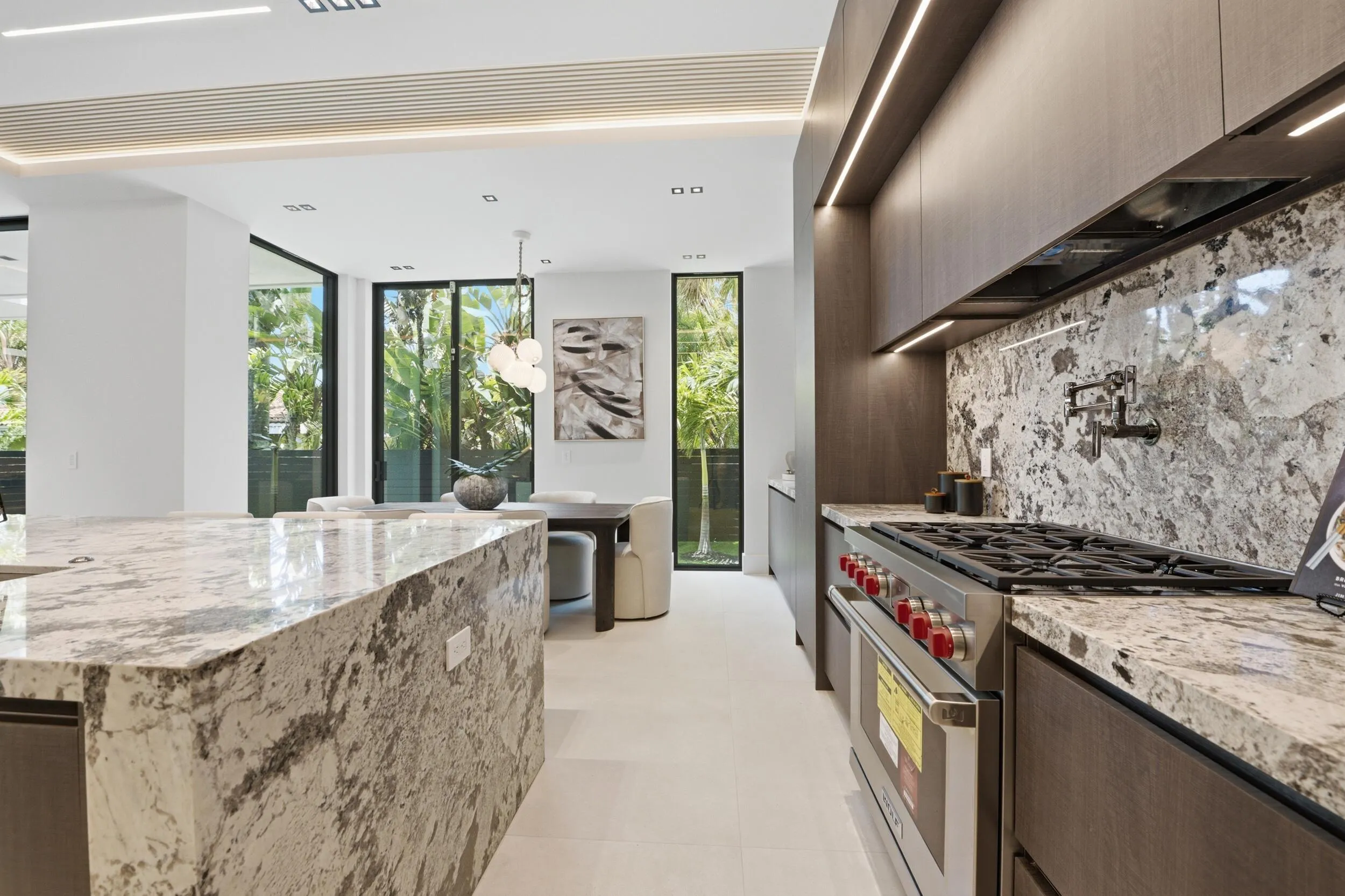 Kitchen featuring a professional-grade range, full-height stone backsplash, custom cabinetry, under-cabinet lighting, and a large stone island
