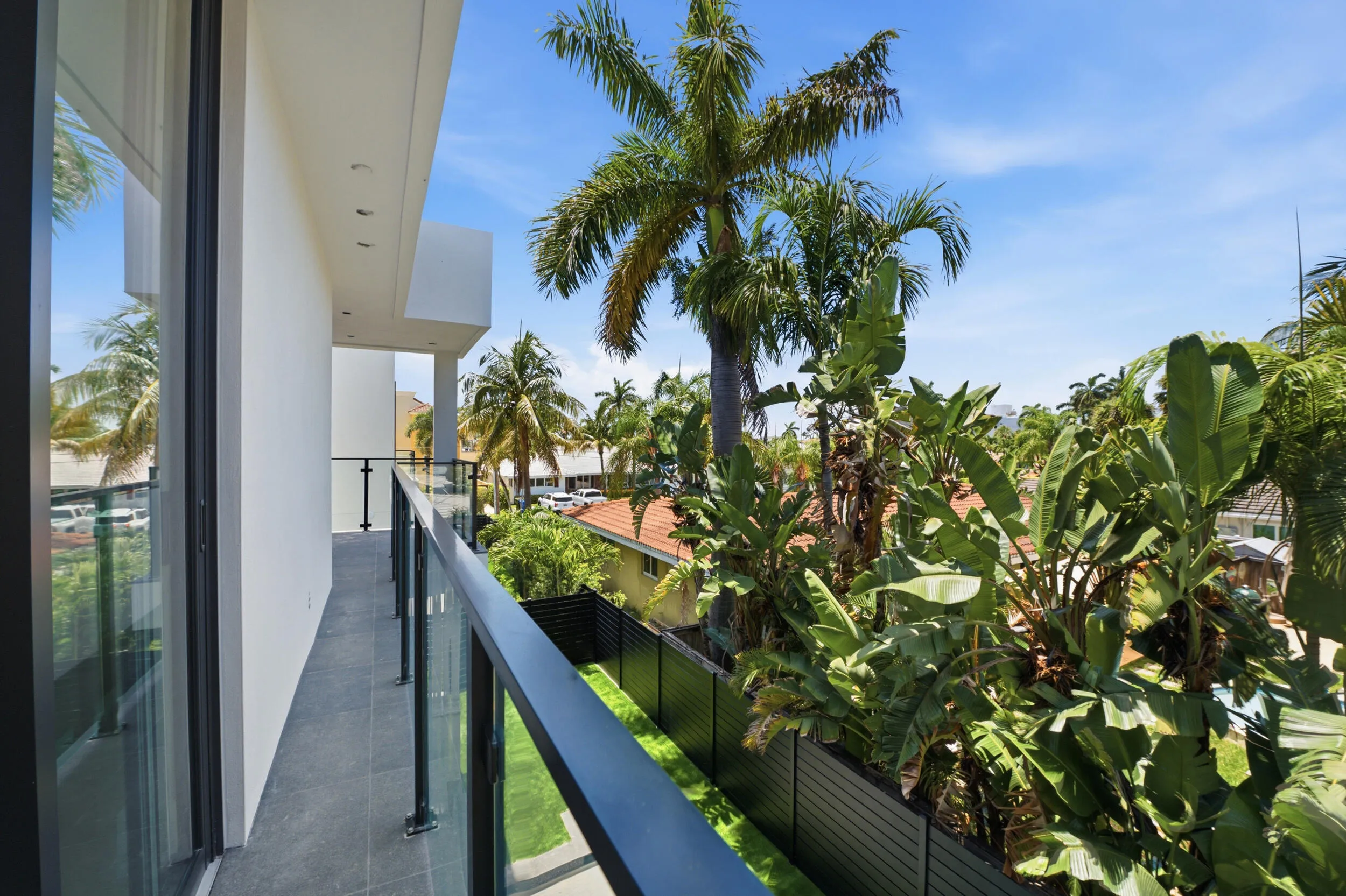 Exterior balcony with glass railings and dark metal top rail, framed by lush tropical foliage