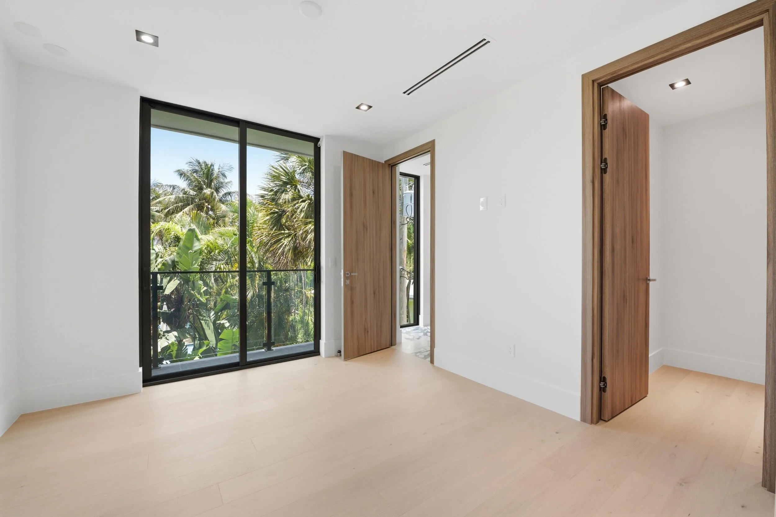 Expansive sliding glass door, glass balcony railing, recessed ceiling lighting, light wood-finish flooring, and wood-finish doors