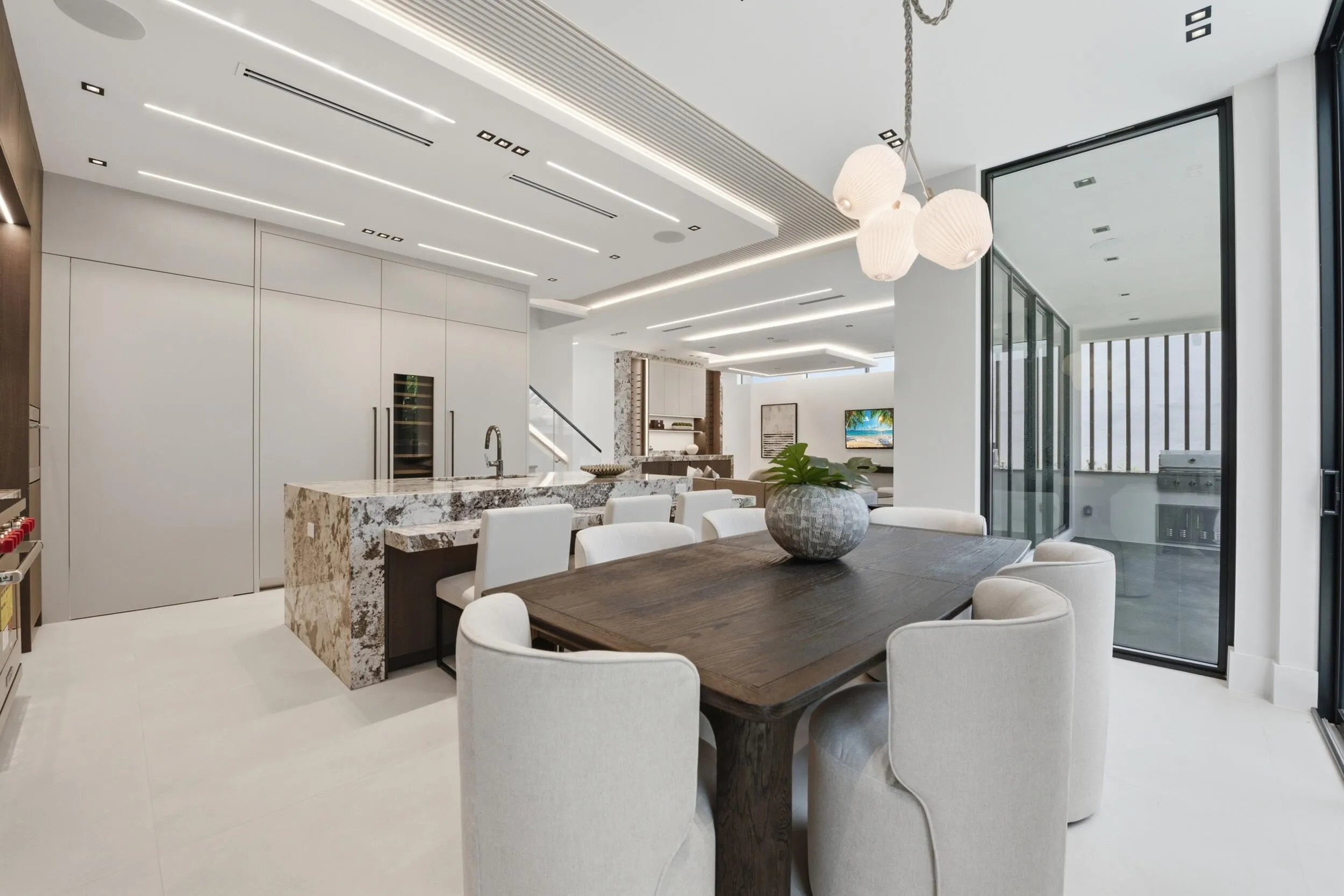 Recessed and linear ceiling lighting, built-in panel-front refrigeration, large kitchen island with stone countertop, integrated wine cooler, and full-height glass doors